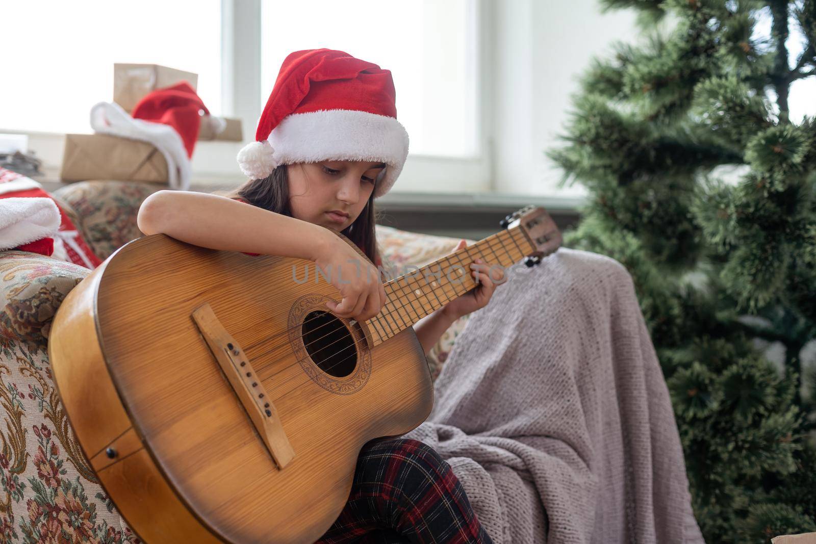Child playing the guitar and singing near a christmas tree by Andelov13