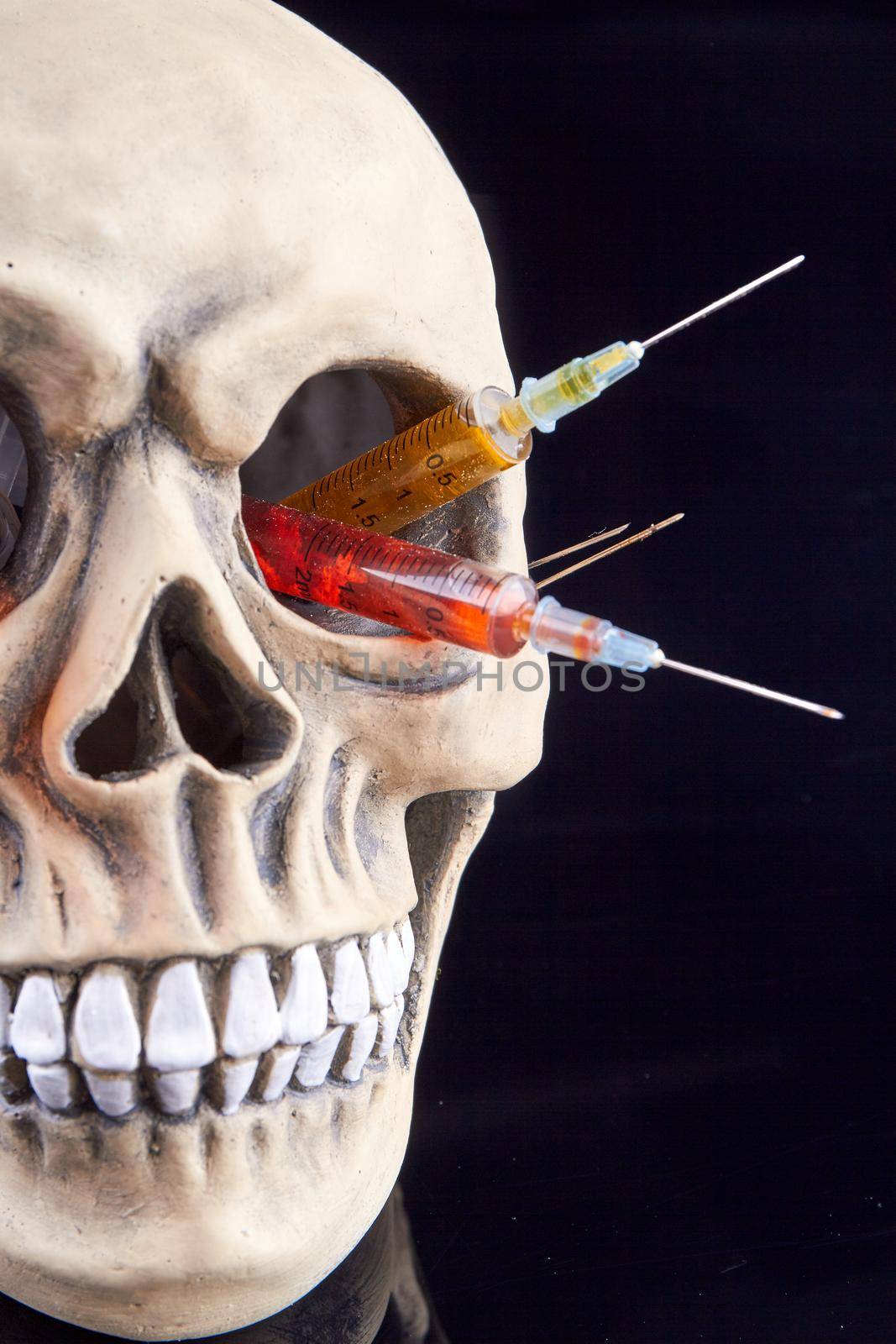 Humans skull with colorful syringes in the eye hole. Isolated on black background.