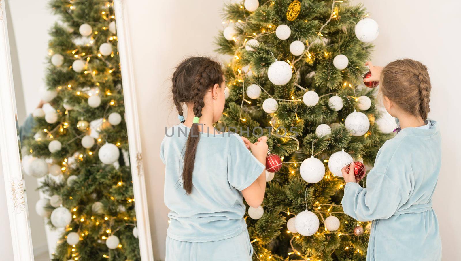 Two cute beautiful girls near the Christmas tree with gifts. New Year. Christmas.