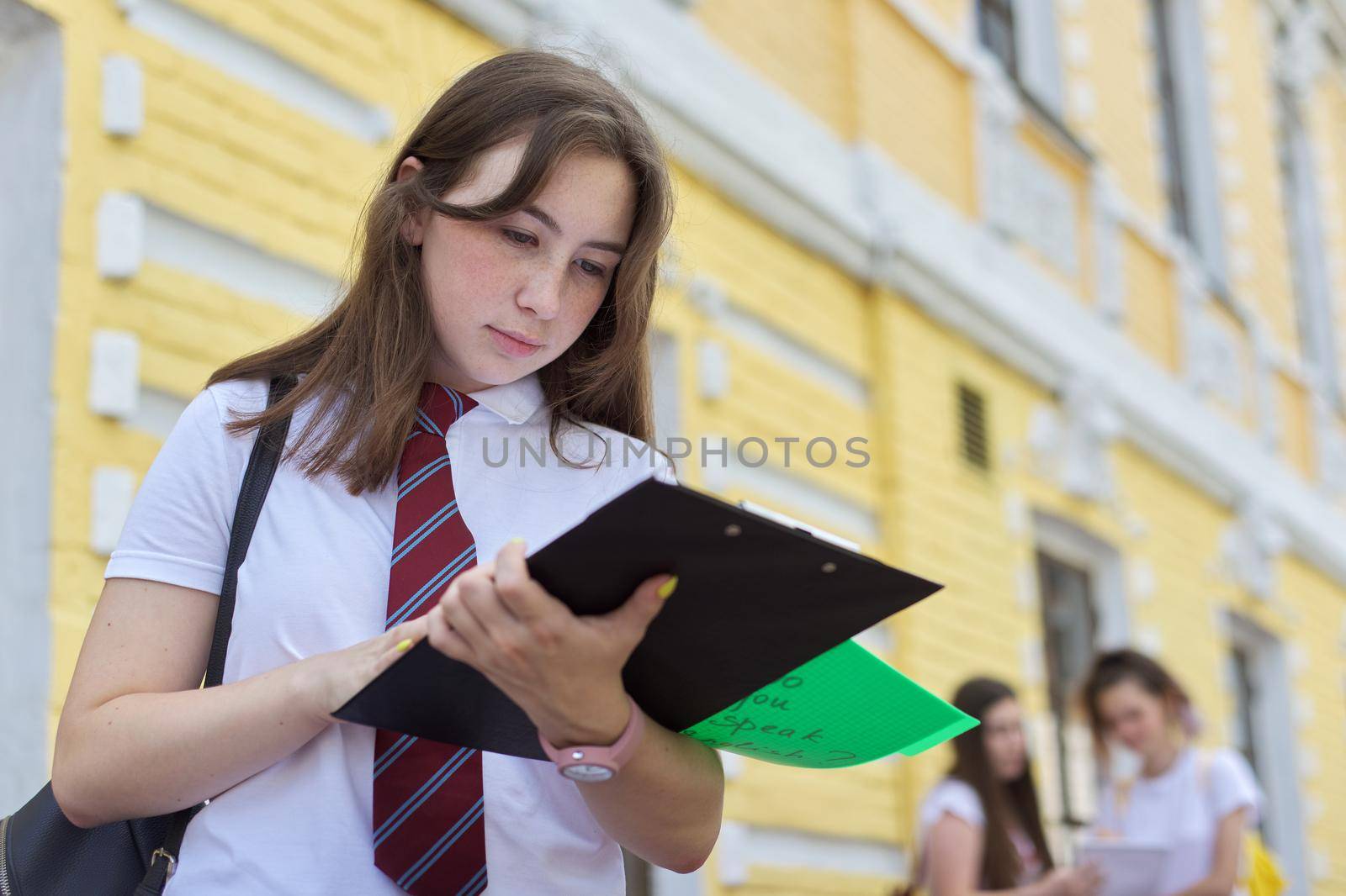 Girl teenager college student posing outdoor in white T-shirt with tie. Background brick building, group of girls students. Beginning of classes, back to college, copy space