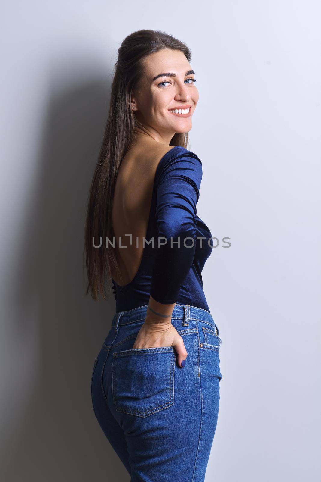 Beauty fashion portrait of young woman in blue body, jeans, white background by VH-studio