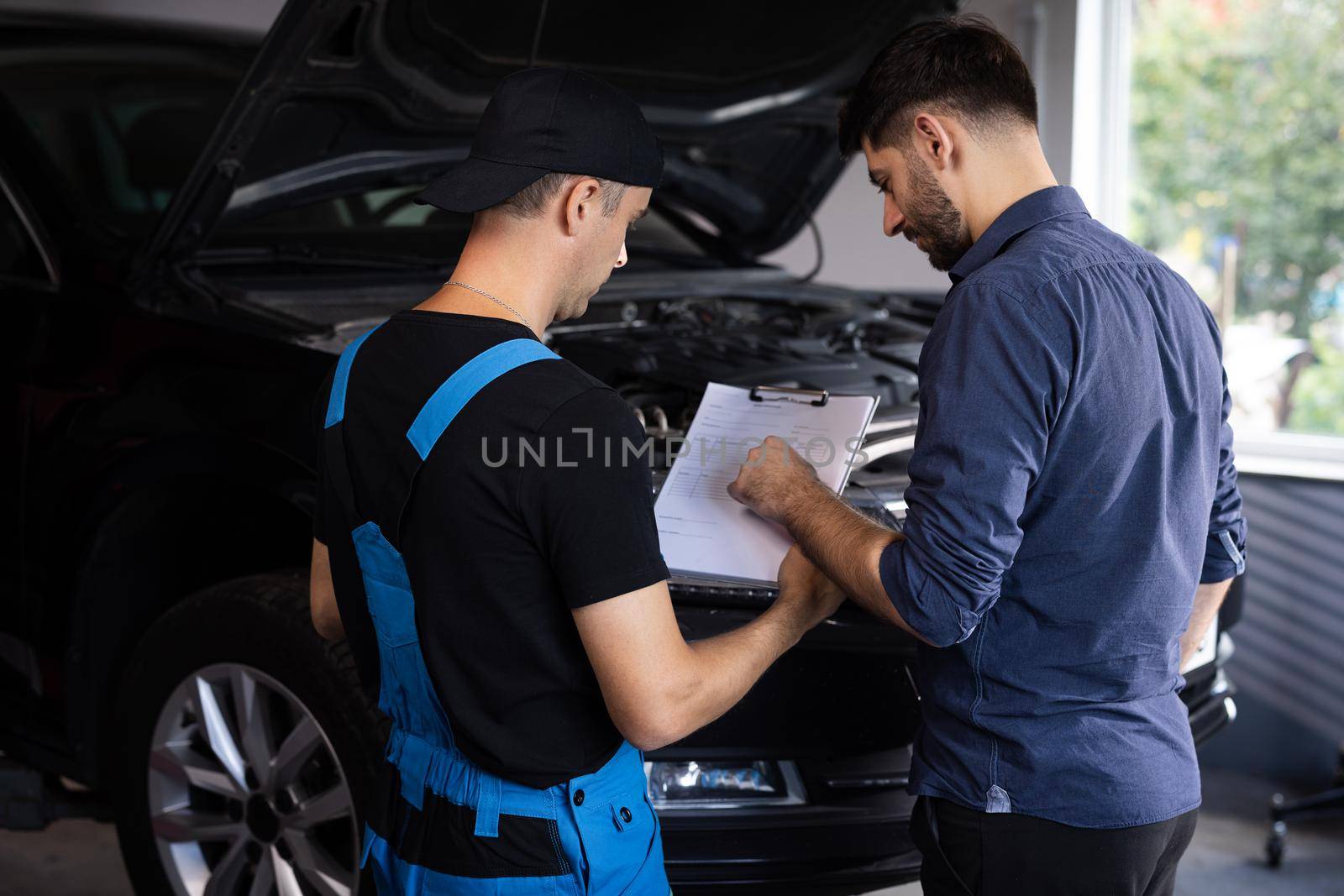 Manager Checks Data on a Tablet Computer and Explains the Breakdown to Mechanic. Car Service Employees Inspect the Bottom and Skid Plates of the Car. Specialist is Showing Info on Tablet. by uflypro