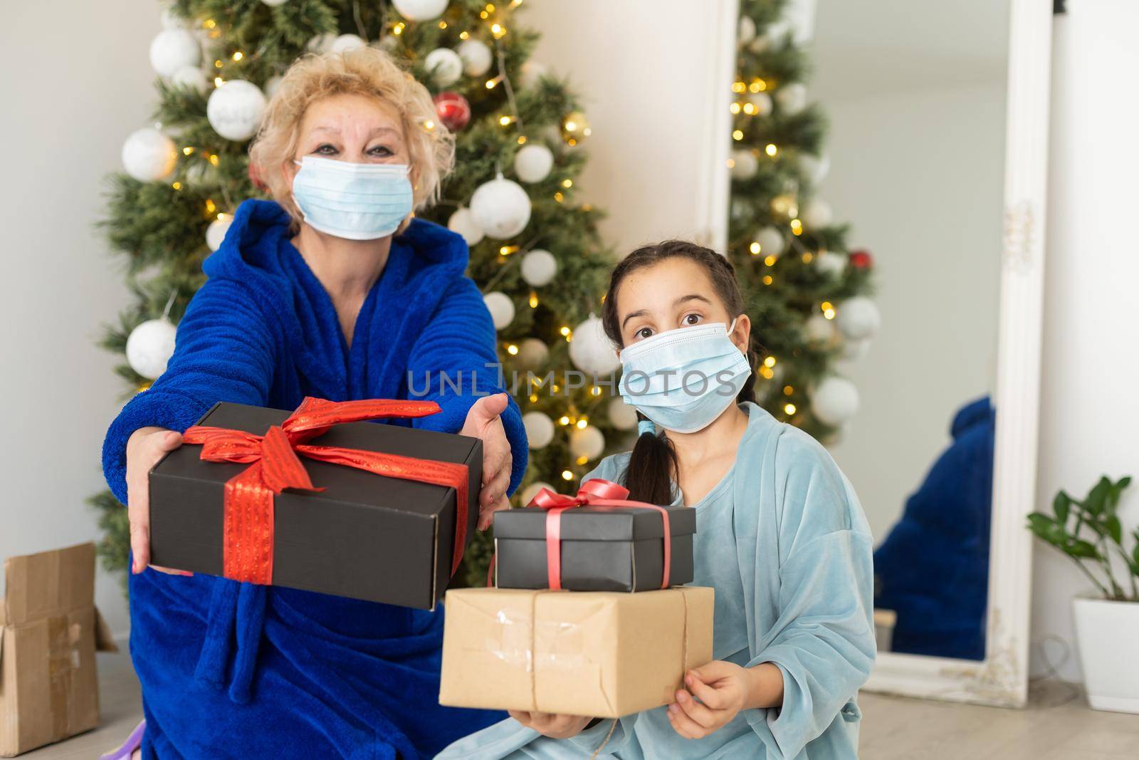 Grandmother and granddaughter n the living room with Christmas decor hugging in medical masks on their faces. A family holiday during the outbreak of coronavirus and disease. New Year by Andelov13