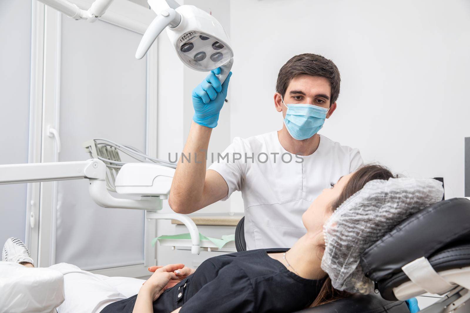 Dentist adjusting dental lamp in dental office. Dentist turning on lamp before treatment by Mariakray