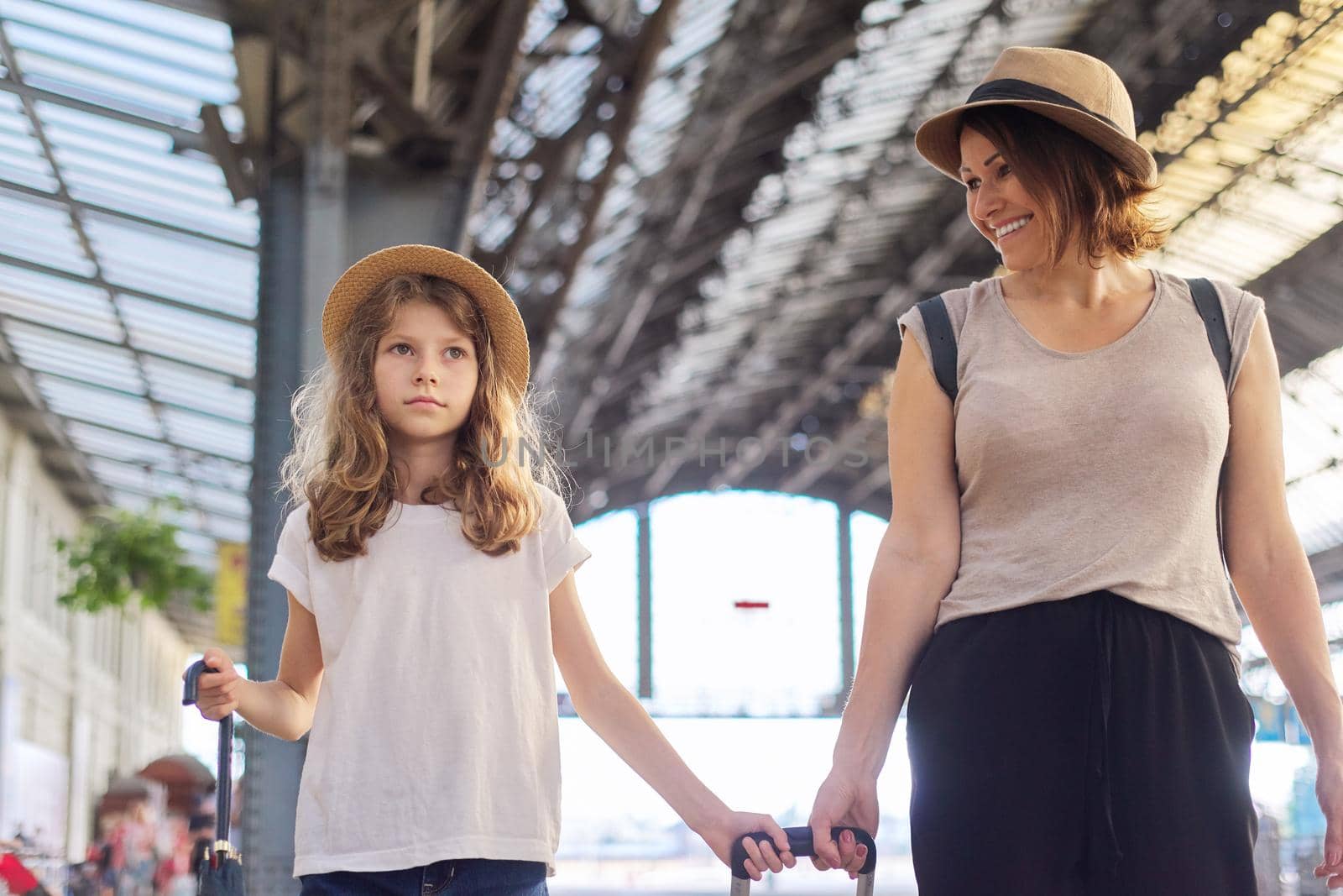 Happy mother and daughter child walking together at railway station with luggage suitcase. Travel, tourism, transportation, family concept