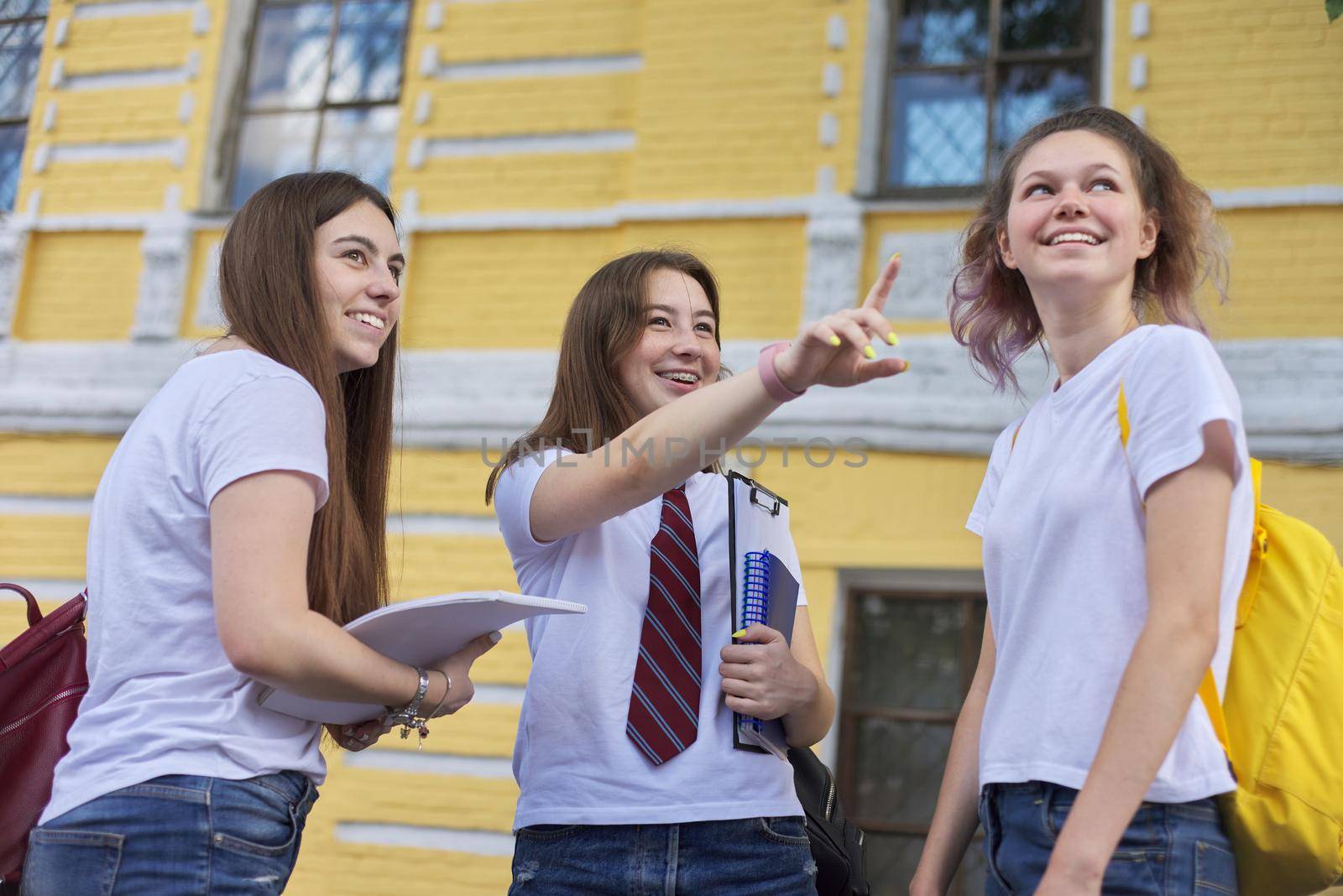 Talking group of student girls, teenage girls college students near brick building. Back to college, start of classes, education, high school