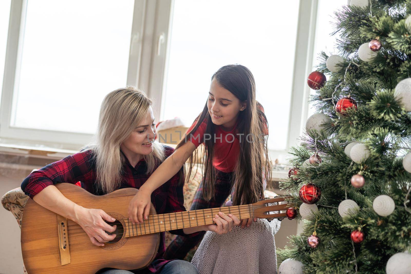 Merry Christmas and Happy Holidays. Mom and daughter decorate the Christmas tree indoors. The morning before Xmas. Portrait loving family close up by Andelov13