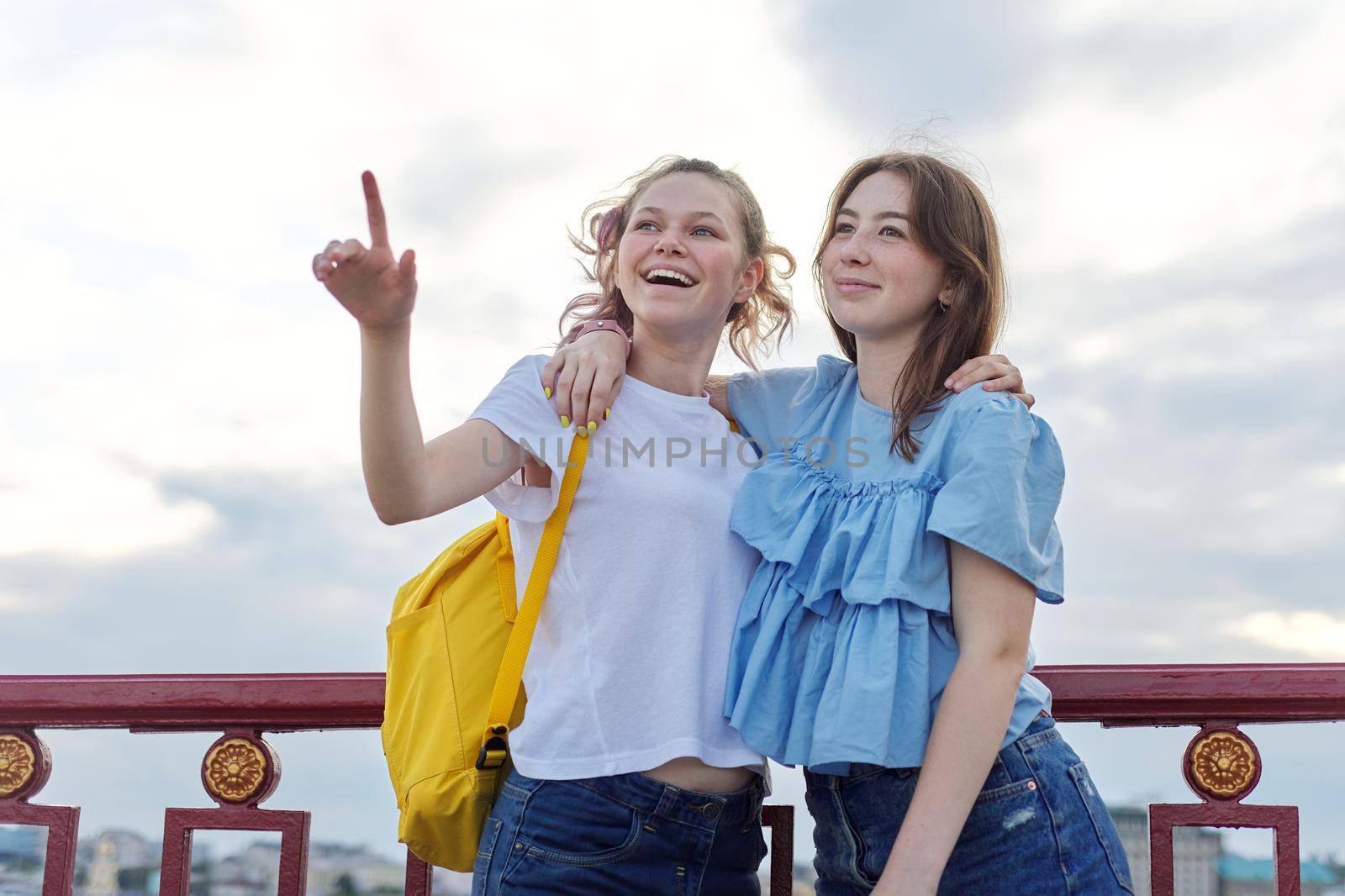 Portrait of two teenage girls friends walking and talking on pedestrian bridge on sunny summer day. Friendship, lifestyle, youth, teens