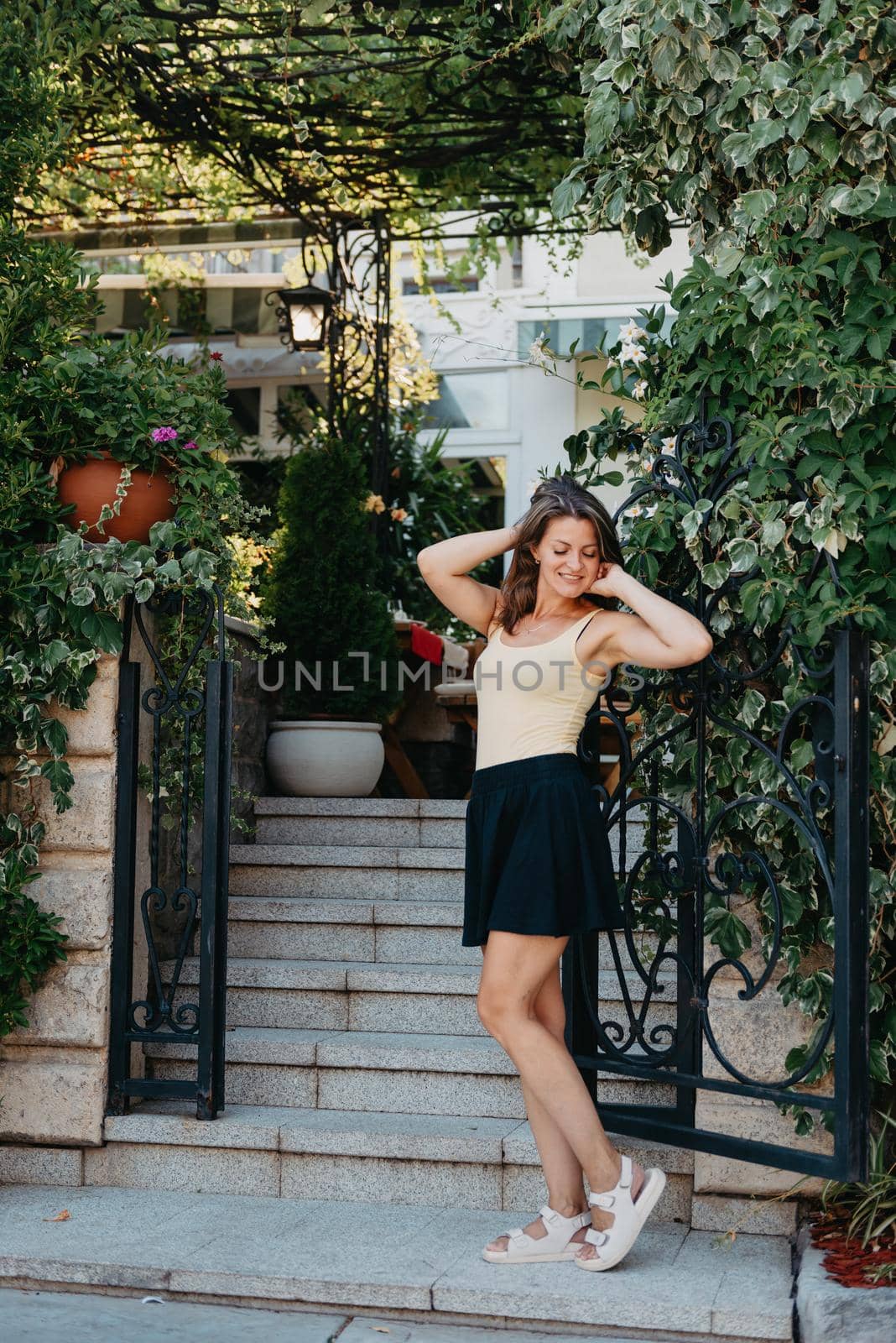 Girl tourist walking through ancient narrow street on a beautiful summer day in MEDITERRANEAN MEDIEVAL CITY , OLD TOWN bUDVA, MONTENEGRO. Young beautiful cheerful woman walking on old street at tropical town. Pretty girl looking at you and smiling