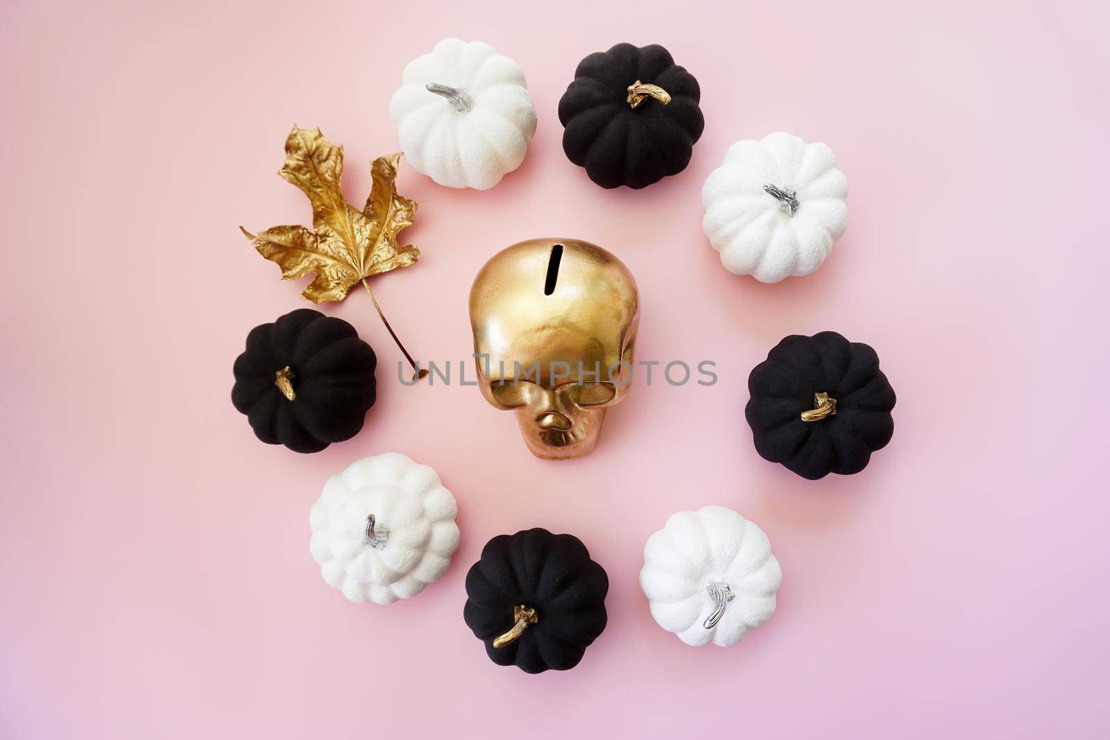 Multicolored pumpkins and a golden skull lie on a pink background. High quality photo