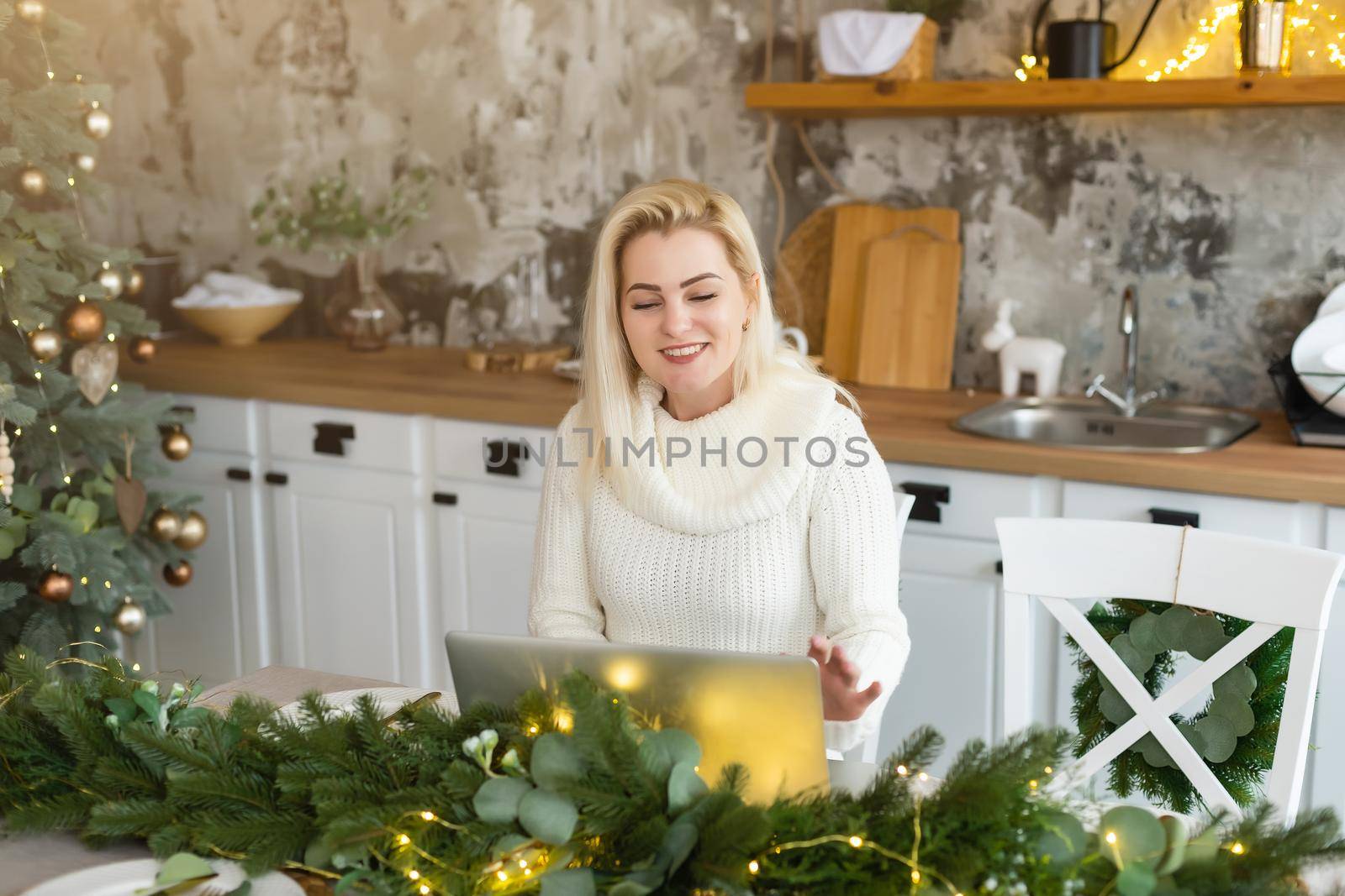 Smiling young woman using laptop near christmas tree.