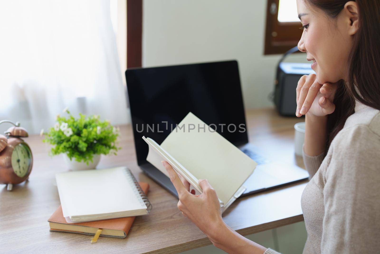 woman sitting at home reading a notebook and using a computer.