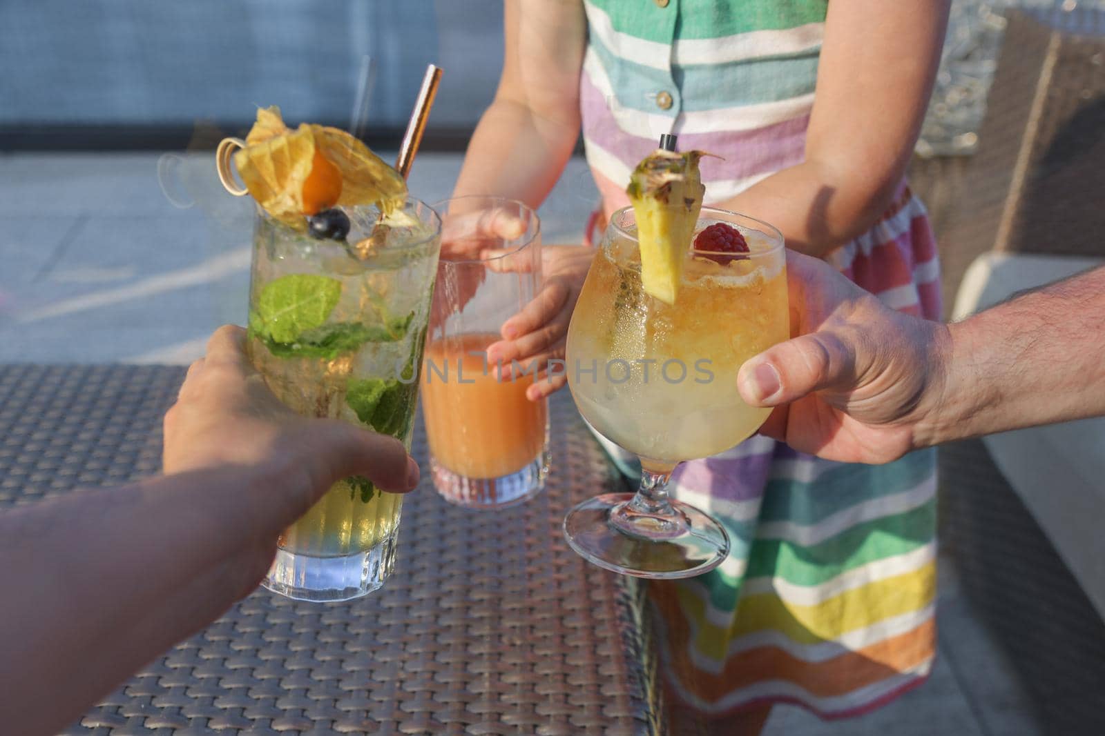 Father mother and daughter clink glasses of cocktails mojito aperol spritz and fruit juice