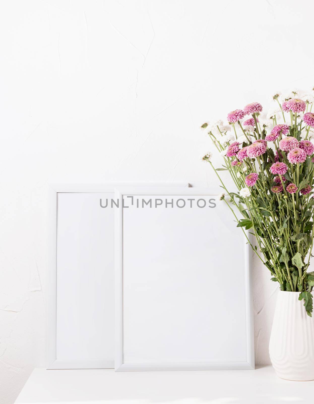 White frame mockup with chrysanthemum flowers in a vase on a white table, mockup design