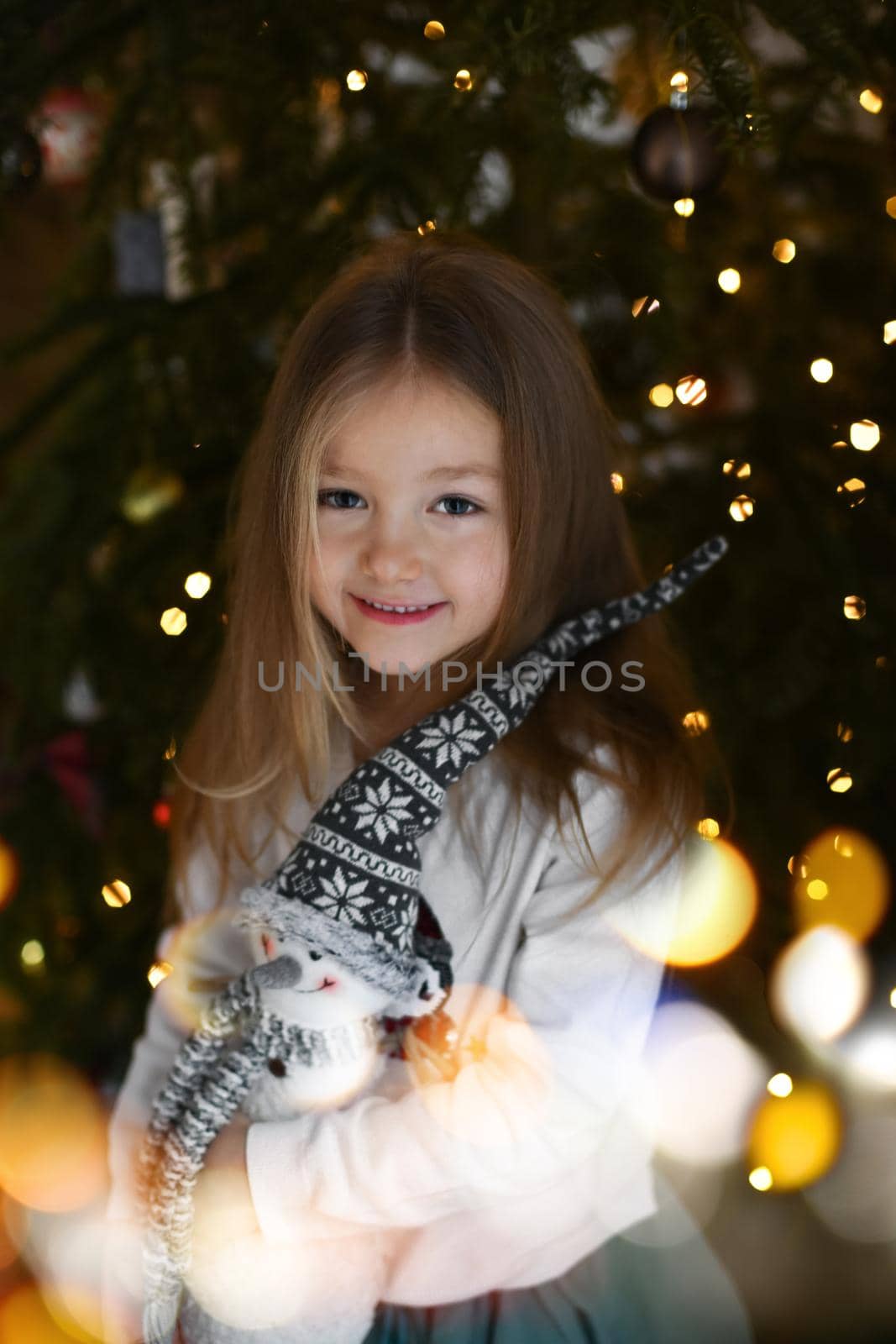 A girl hugging a snowman toy near a Christmas tree