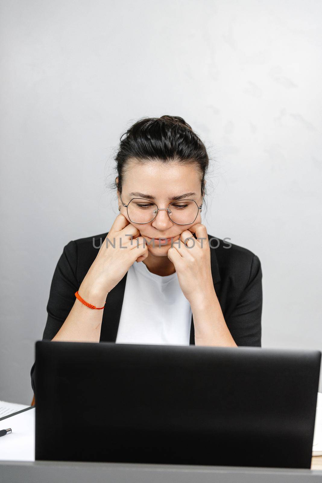 Serious thoughtful young businesswoman economist pondering in the office, wearing a jacket and T-shirt and glasses.