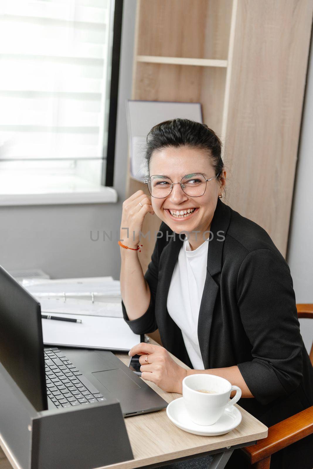 A young businesswoman employee or manager uses a computer, looks at a customer or employee and smiles. Hybrid work empty office by gulyaevstudio