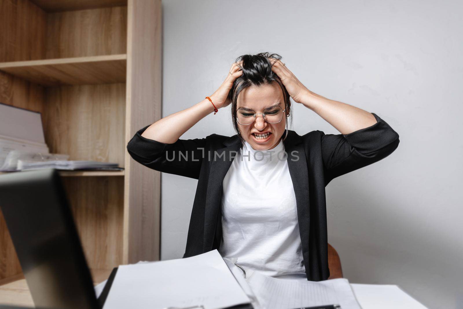 stress at work. The girl worker in the office is holding her head in anger and frustration. Stress in the office. Bad atmosphere. Life in a non-office concept of a new job. Hybrid work.