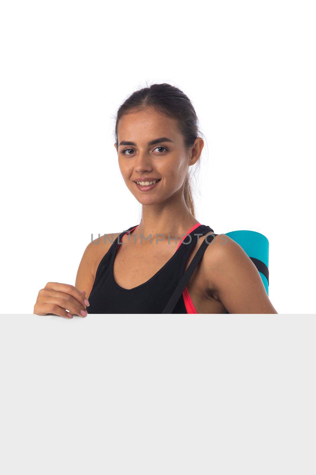 Healthy hispanic fitness girl with rolled gymnastics yoga mat and blank banner isolated on white background