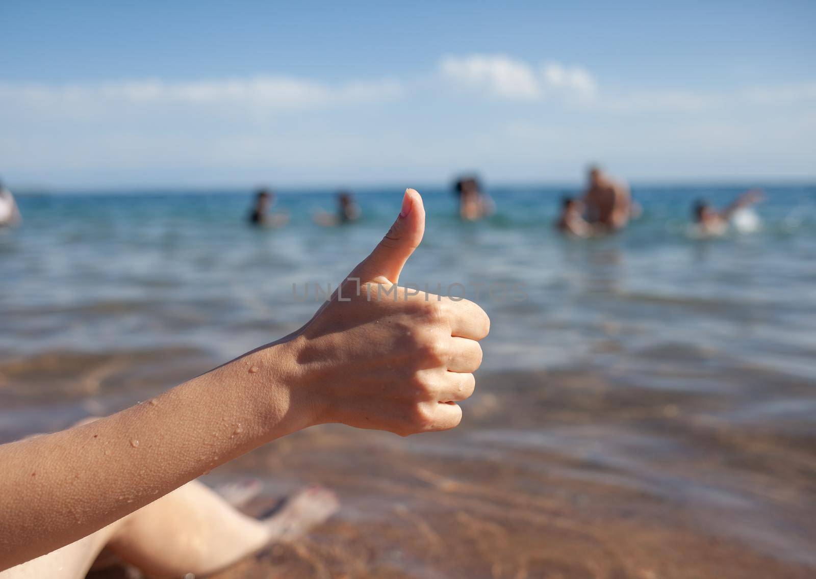 Female hand thumbs up on sea and sky background closeup. Woman showing ok sign on shoreline coastline. Body language, communication concept. Holiday, vacation, summer is coming conceptual photo.