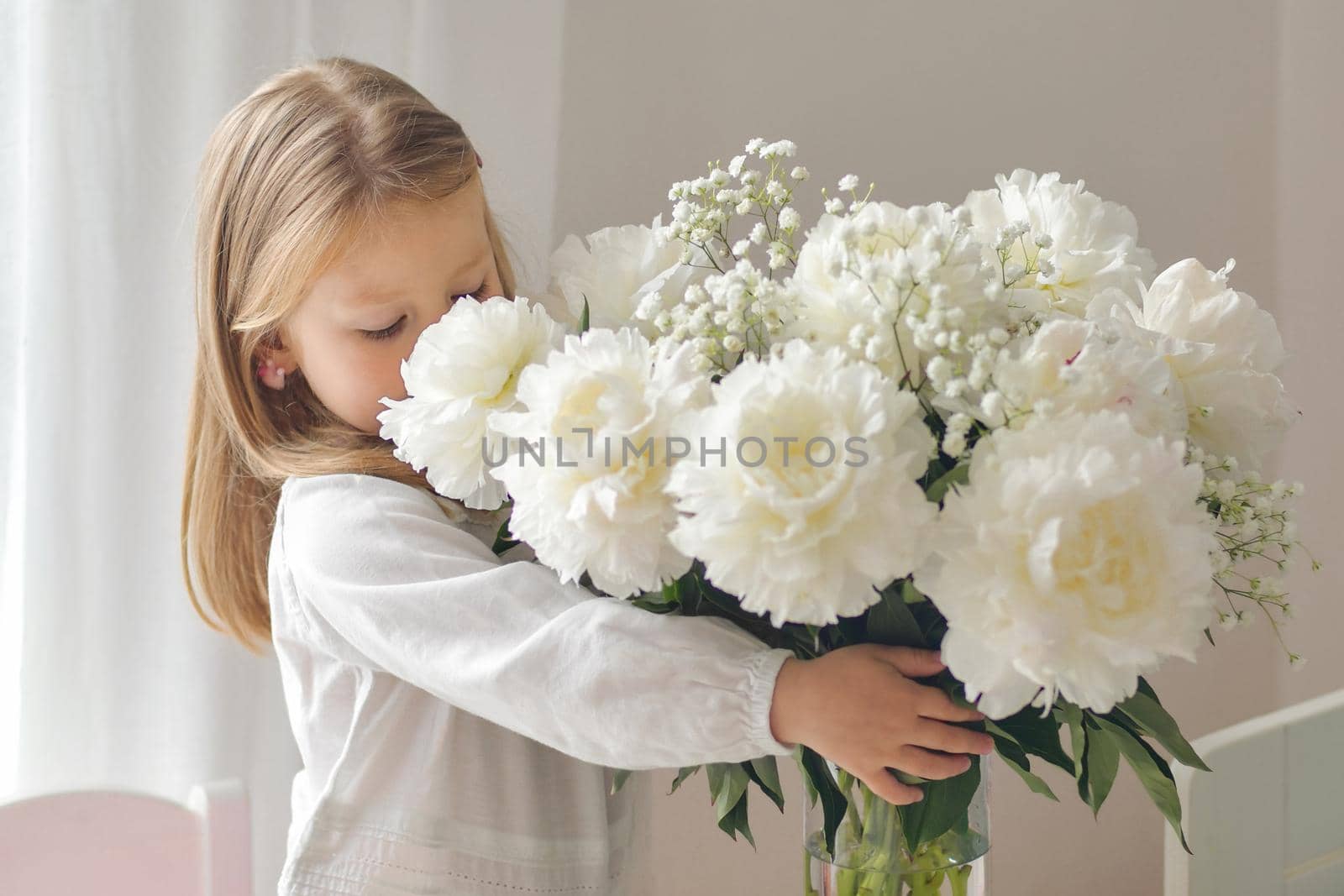 A little girl smelling a bouquet of the white peonies