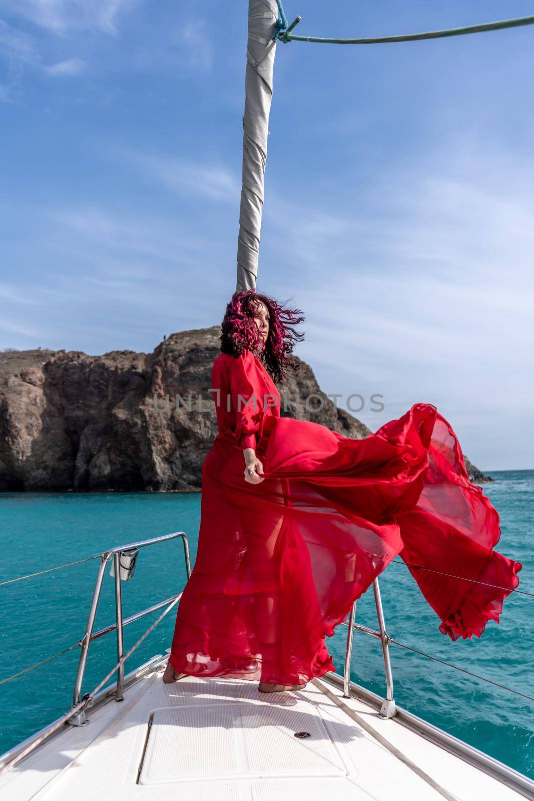 Attractive middle-aged woman in a red dress on a yacht on a summer day. Luxury summer adventure, outdoor activities. by Matiunina