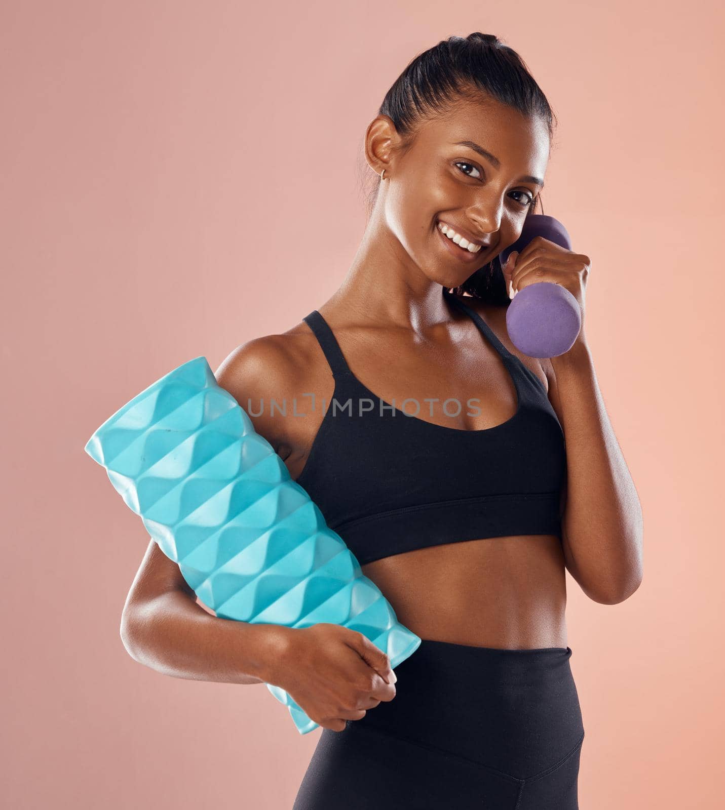 Smiling, healthy and slim female fitness instructor, holding weights and exercise equipment or tools for workout. Beautiful woman athlete with a fit body in gym sportswear against studio background by YuriArcurs