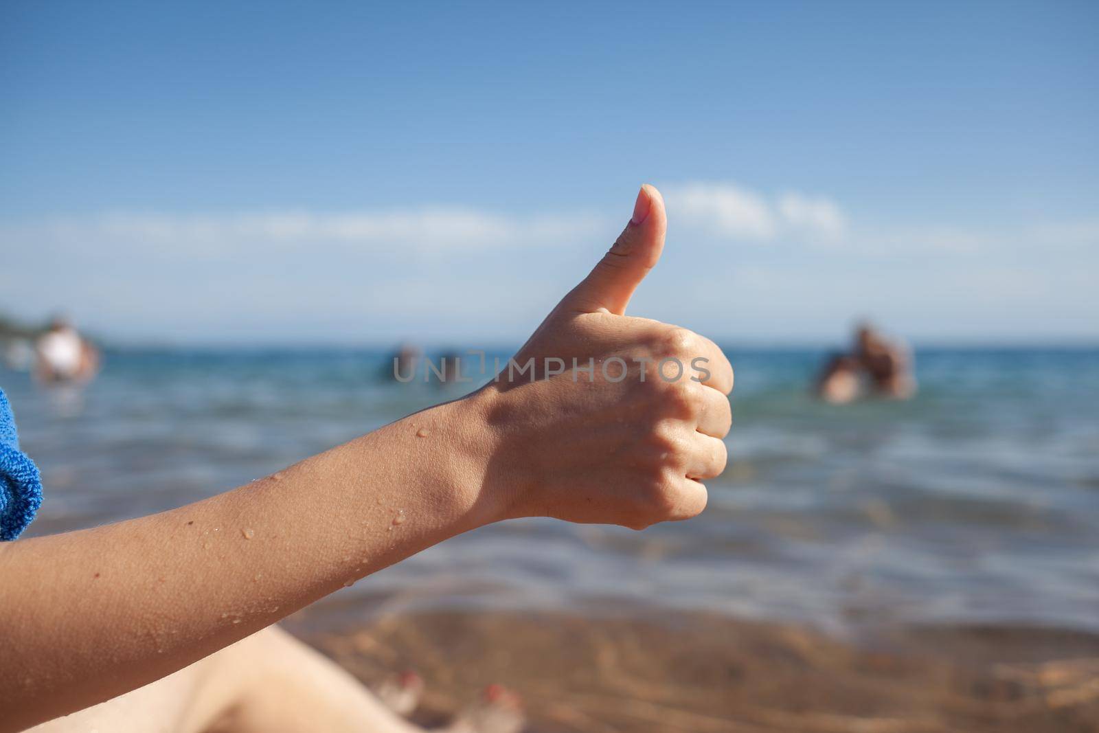 Female hand thumbs up on sea and sky background closeup. Woman showing ok sign on shoreline coastline. Body language, communication concept. Holiday, vacation, summer is coming conceptual photo.