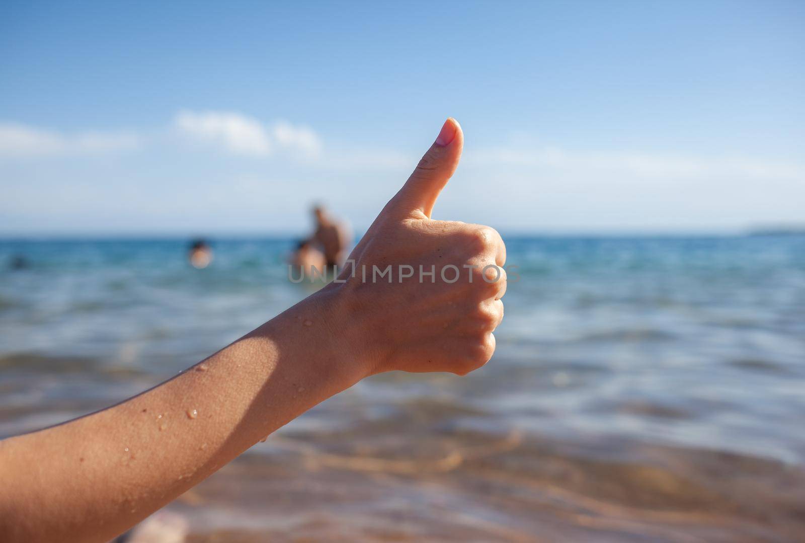 Female hand thumbs up on sea and sky background closeup. Woman showing ok sign on shoreline coastline. Body language, communication concept. Holiday, vacation, summer is coming conceptual photo.