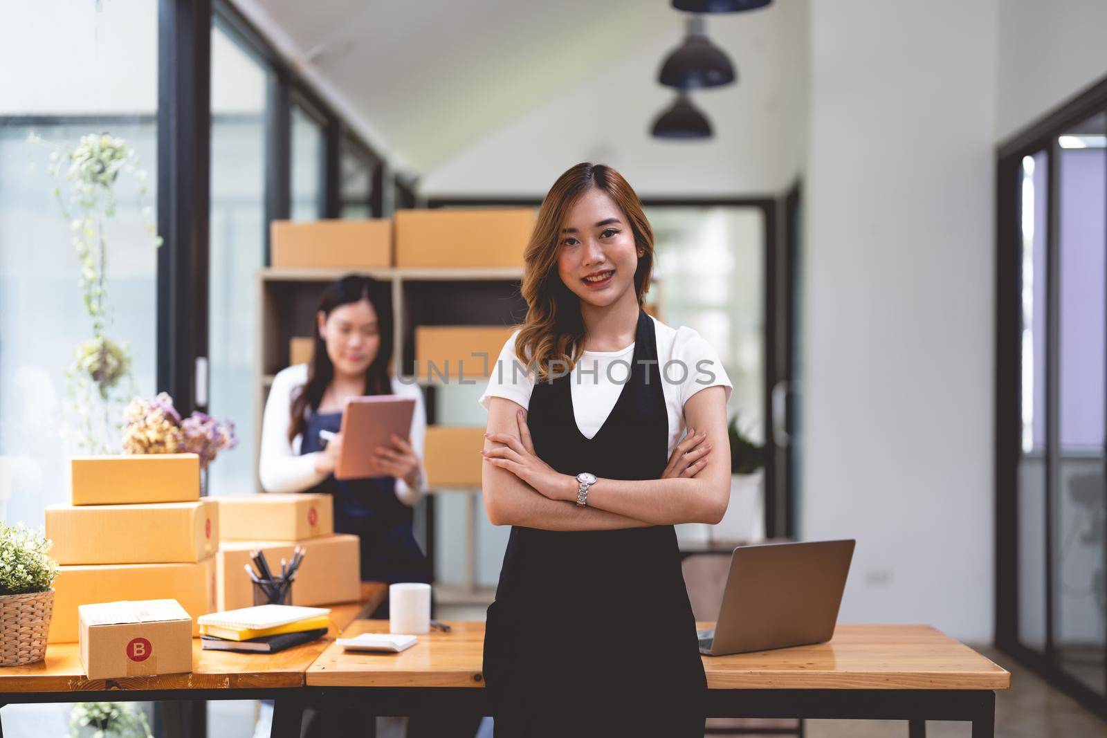 Young asian woman holding delivery boxes at small business smiling looking to the camera.