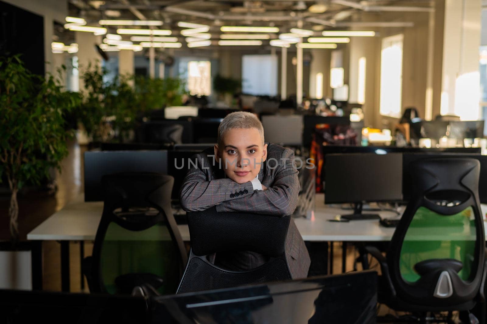 Pensive young woman with short hair sits in armchair in office