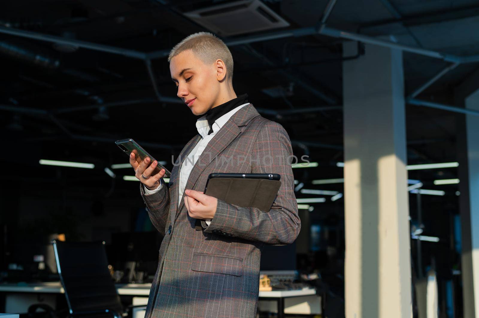 Pensive young woman with short hair uses mobile phone in office