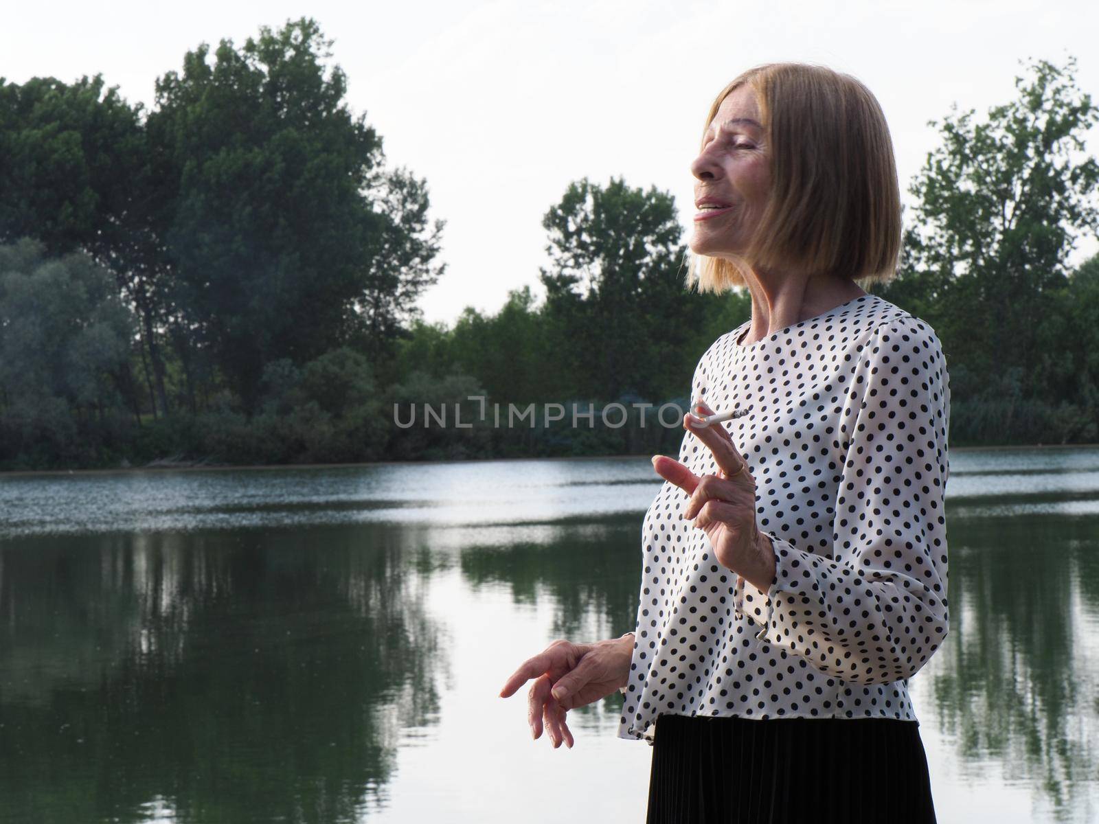 female pensioner having fun and smoking a cigarette in a park - aging free and wellness concept