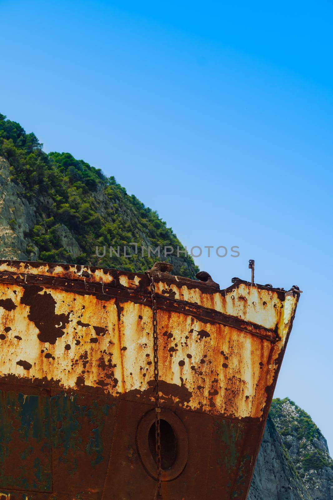 Day low angle view of abandoned rusted shipwreck with bow visible at Zakynthos island Greece, against blue sky background.