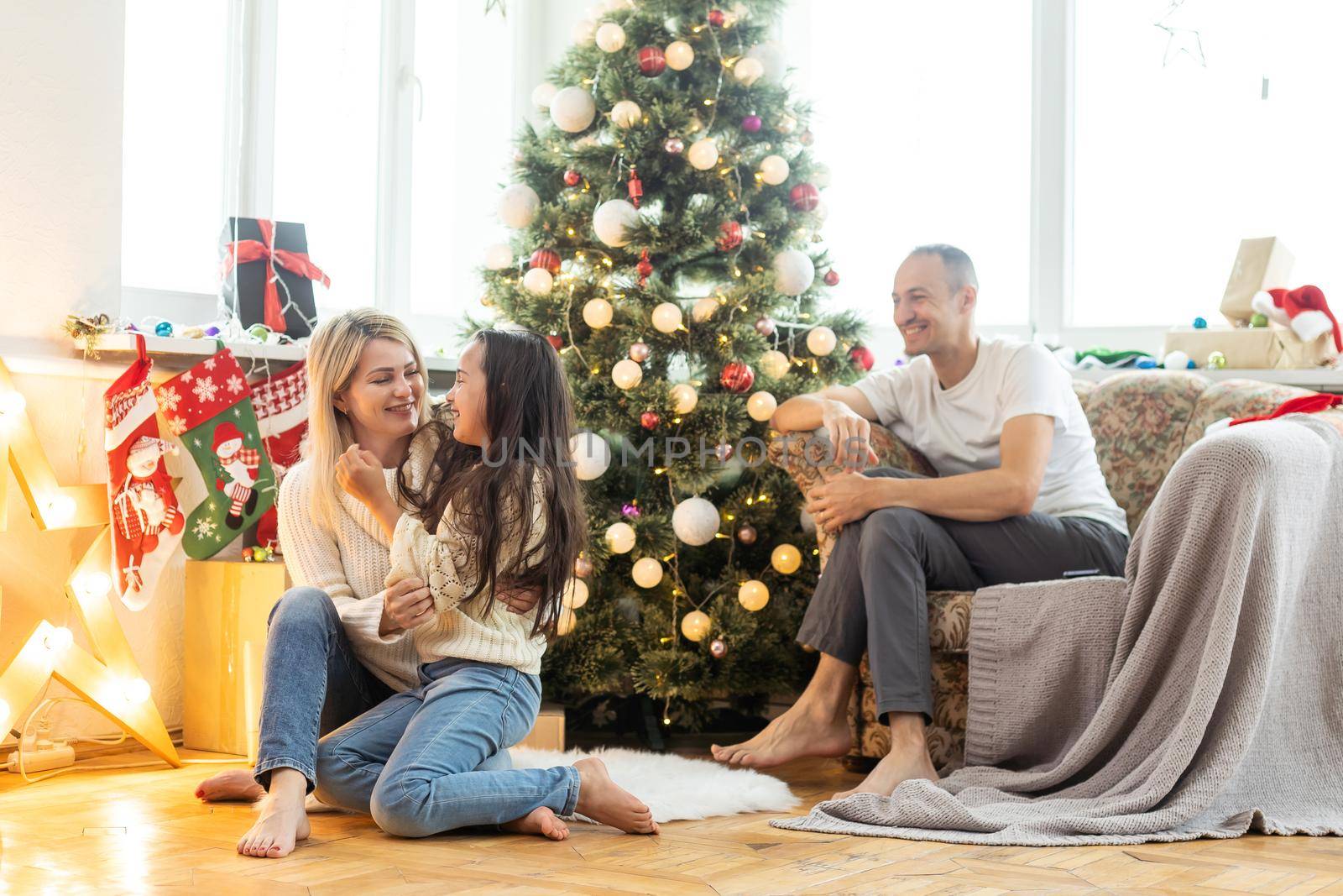 Beautiful young family enjoying their holiday time together, decorating Christmas tree, arranging the christmas lights and having fun