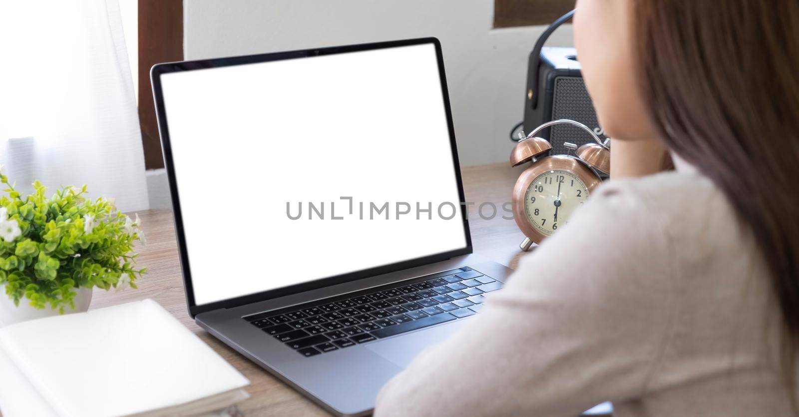 Mockup image of a woman using and typing on laptop with blank white desktop screen on wooden table.