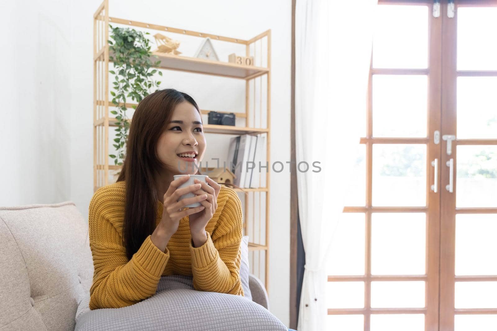 Young asian woman drinking coffee on a sofa bed at home by wichayada