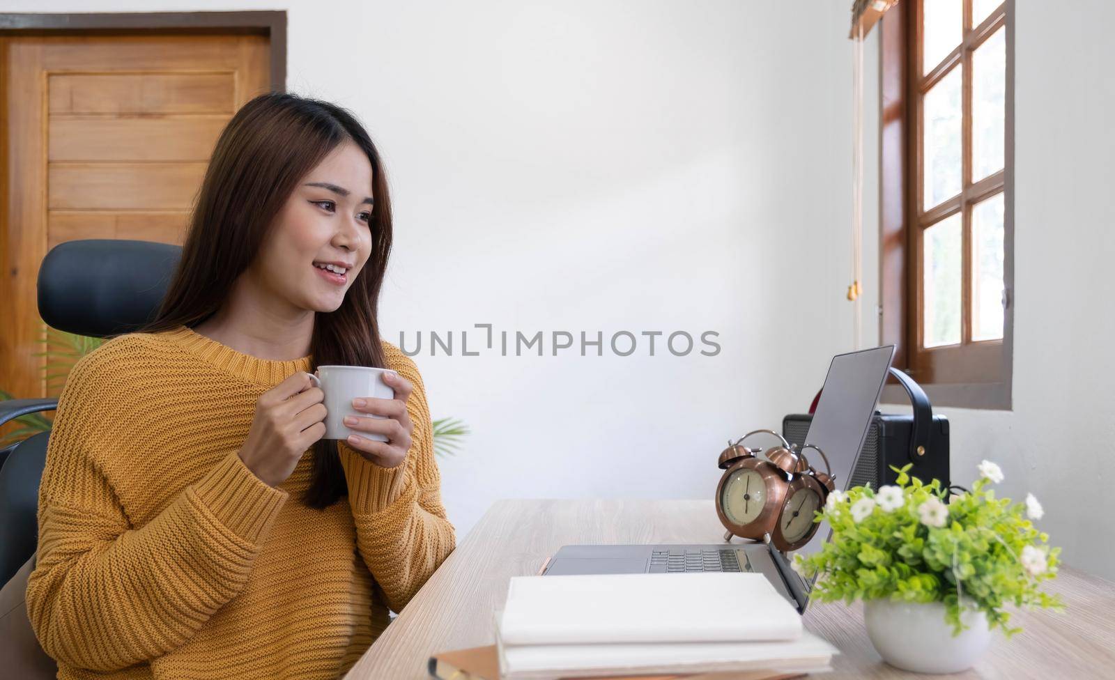 Beautiful young smiling asian woman working on laptop and drinking coffee in living room at home. Asia business woman working document finance and calculator in her home office. Enjoying time at home..