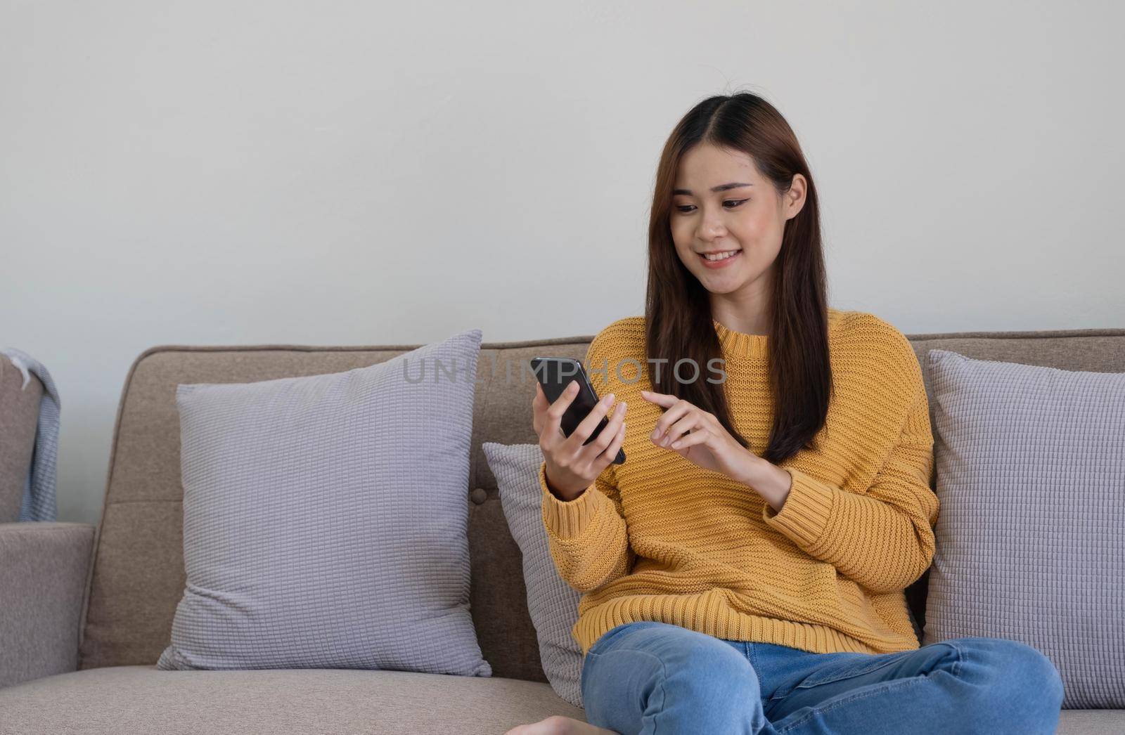 Happy asian woman using mobile phone. Smiling young female using app shopping online, ordering delivery relax on sofa at home..