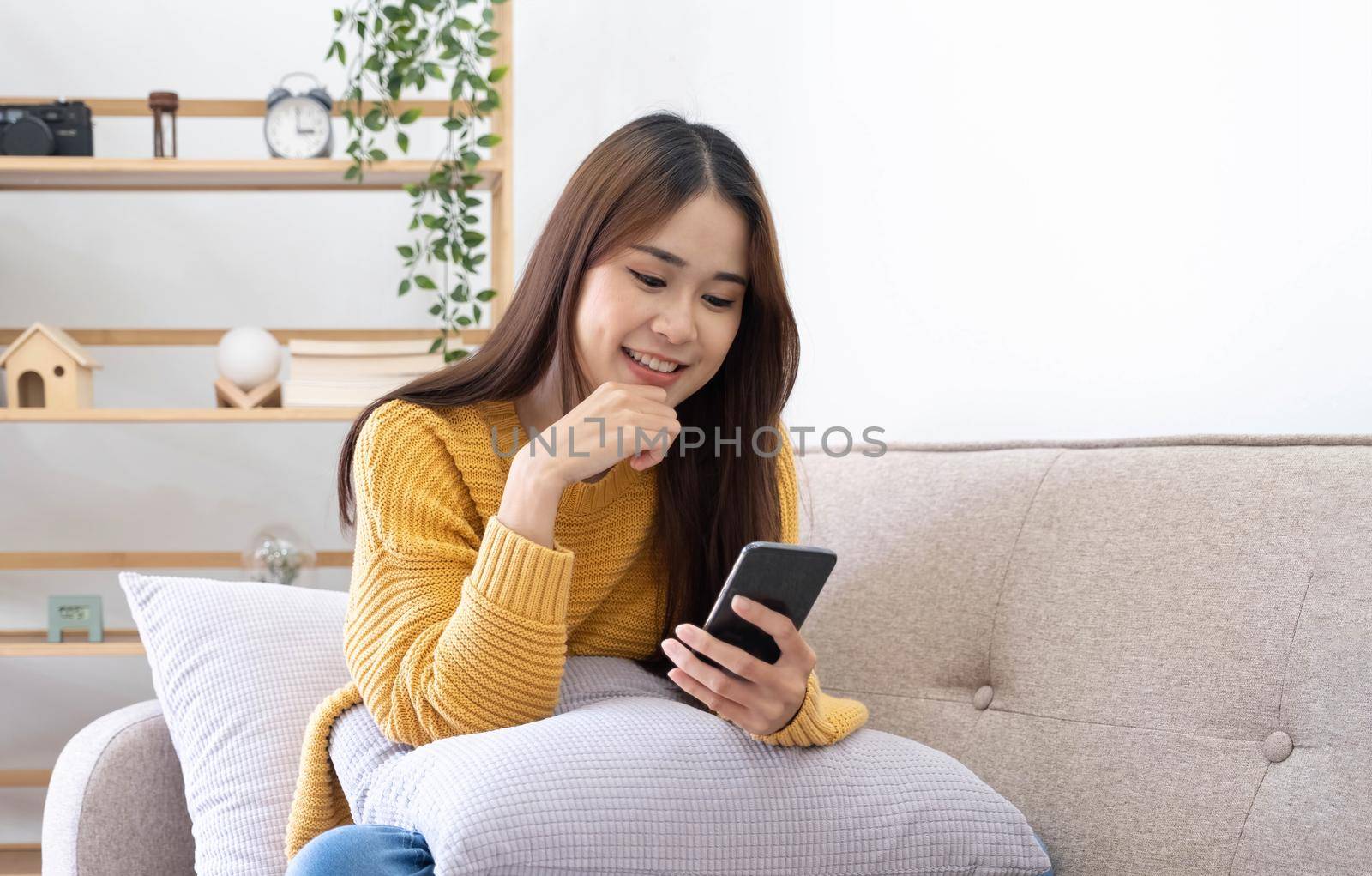 Free time. Asian girl checking social networks on phone, resting on sofa, panorama with free space.