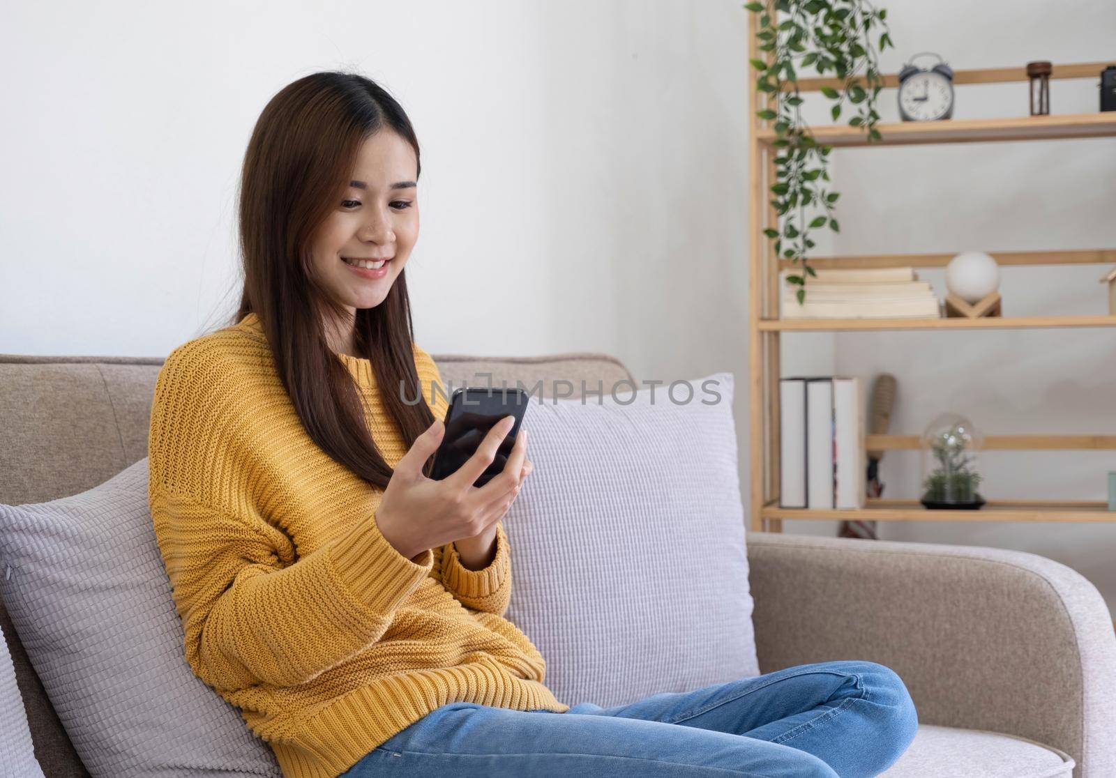 Happy asian woman using mobile phone. Smiling young female using app shopping online, ordering delivery relax on sofa at home..