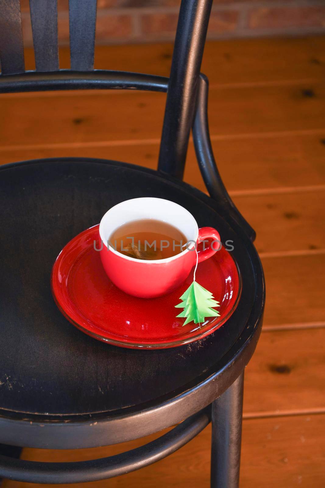 A red cup with tea is wrapped in a warm Christmas sweater, a tea bag label in the form of a green Christmas tree. High quality photo