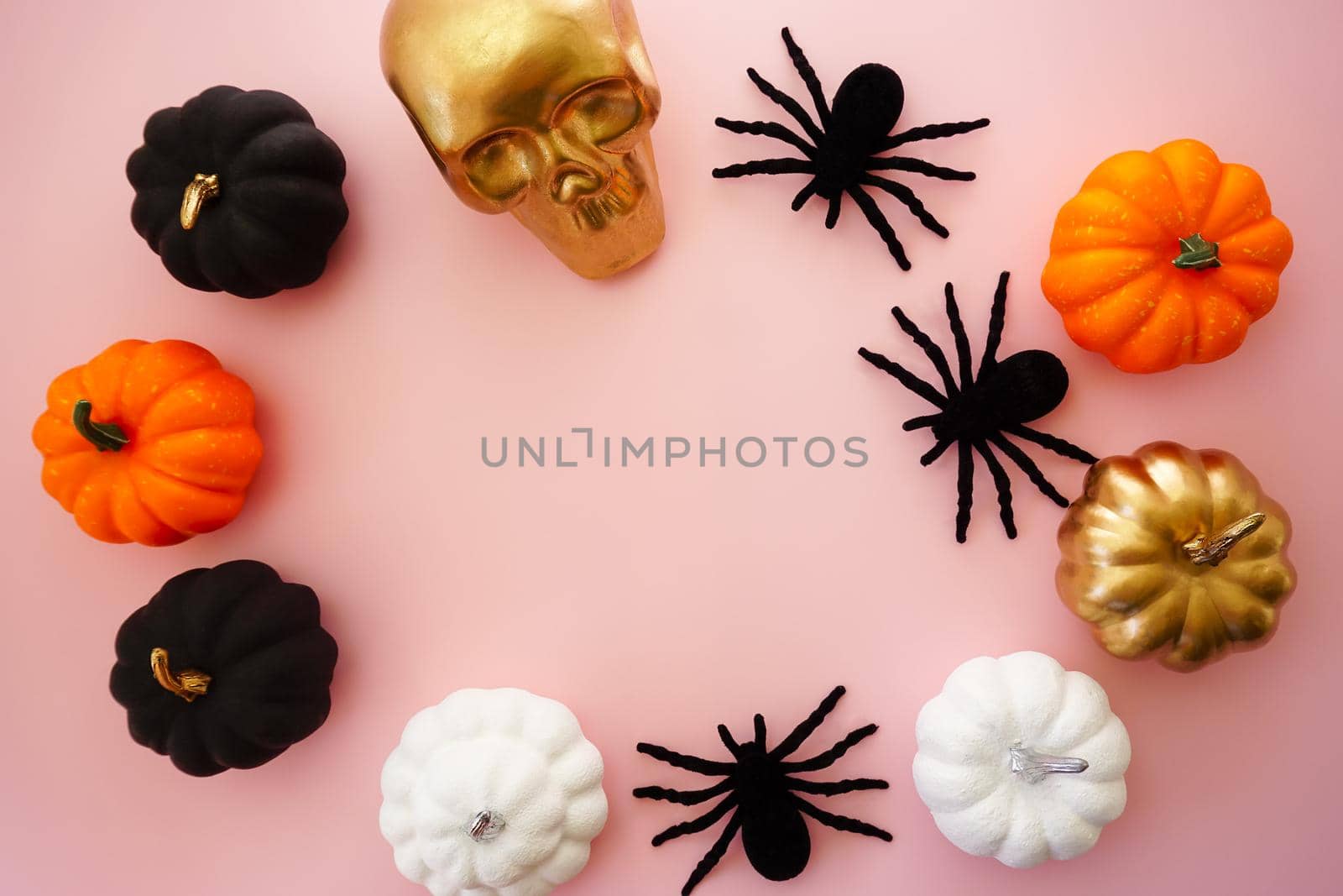 Multicolored pumpkins, a golden skull and black spiders lie on a pink background by Spirina