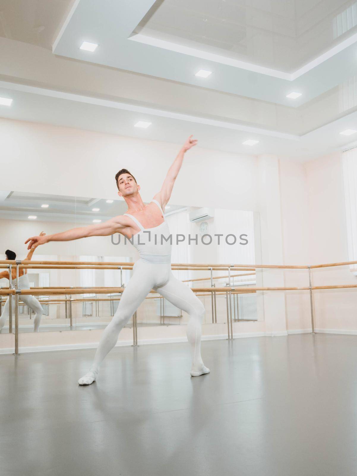 Young handsome male dancer practicing in classical ballet in small studio with mirrors. Man in white tights. Professional choreographer is working on creating performance.