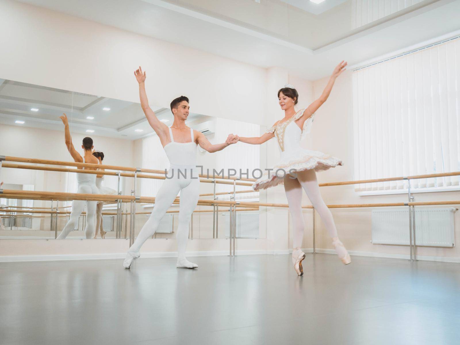 Training before performance. Man dancing classical ballet, he rotating pretty woman in white tutu dress in gym or ballet hall. Couple perform sensual dance. Minimalism interior.