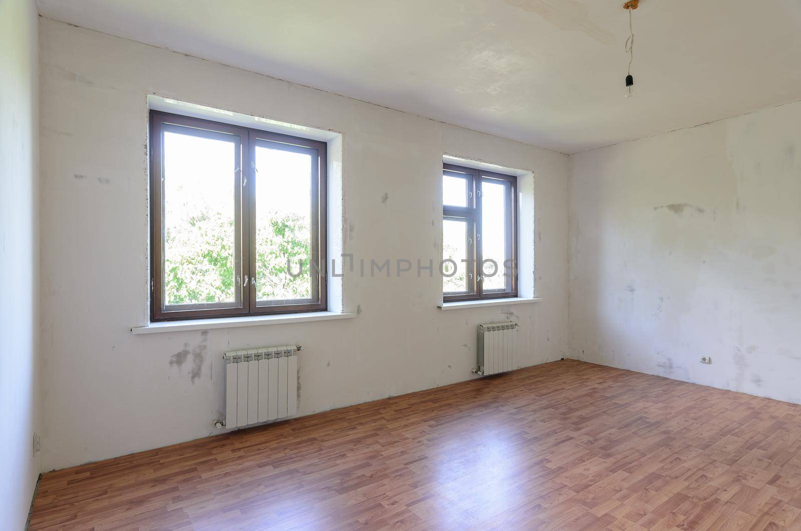 The interior of an empty room during renovation, there are two large windows in the room, radiators under them a