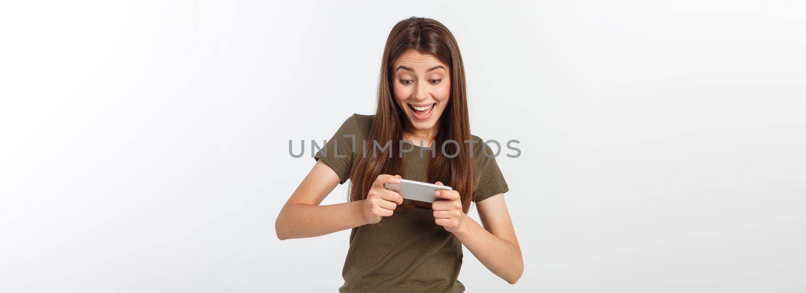 Happy attractive brunette girl joying win in video game on smartphone, isolated over grey background.