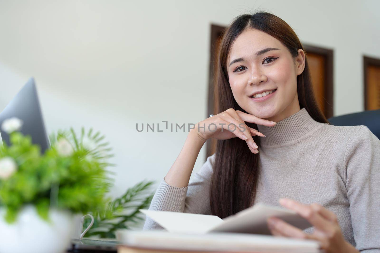 woman sitting at home reading a notebook and using a computer.