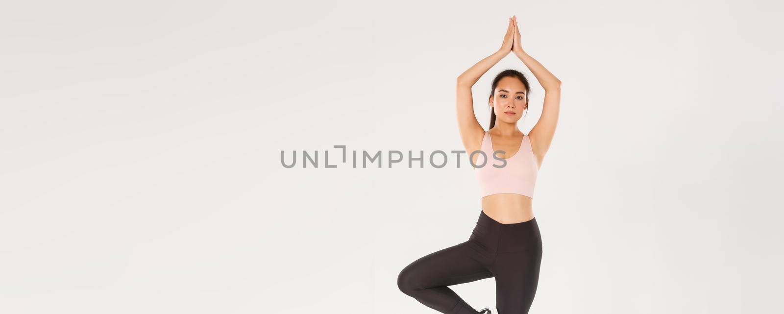 Sport, gym and healthy body concept. Full length of focused, slim brunette asian girl in fitness outfit practice yoga. Girl lifting arms above head and standing in asana pose, white background by Benzoix
