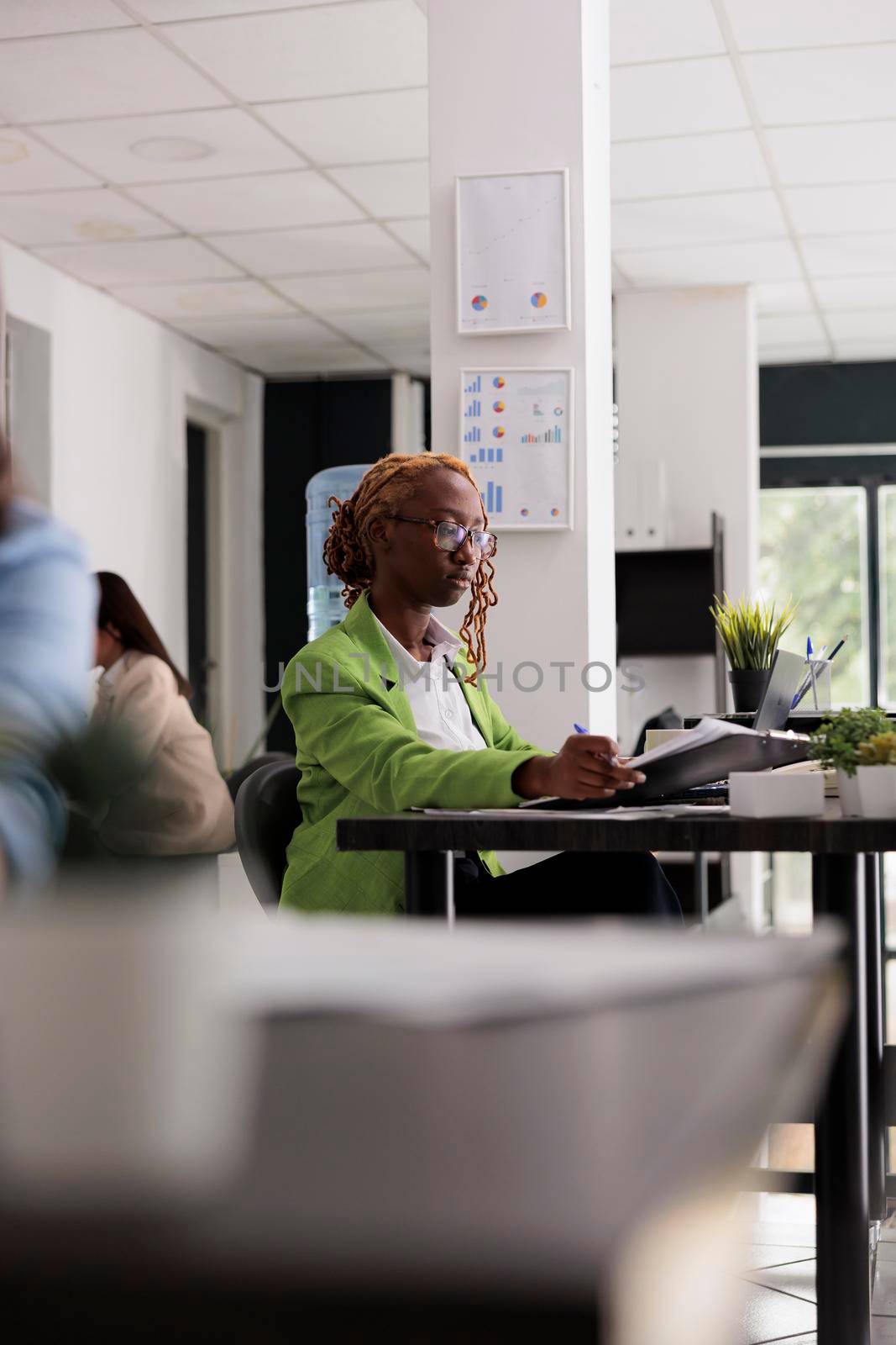 Employee working with business documents, analyzing financial report in office open space, woman sitting at workplace desk. Young woman looking at company papers, side view